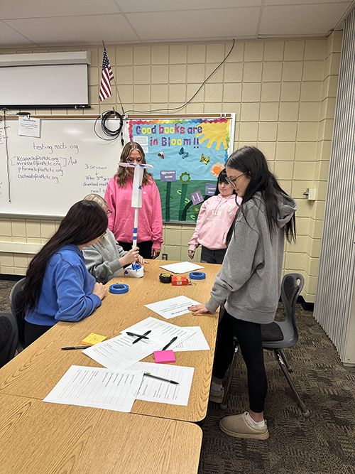 Group of girls working together at a desk with papers and pens