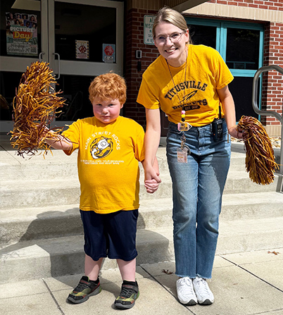 ECLC teacher with a student outside posing for a picture with cheerleading pom-poms