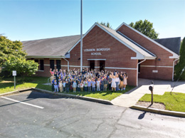 Students and staff waving to the camera from outside the front of the school building