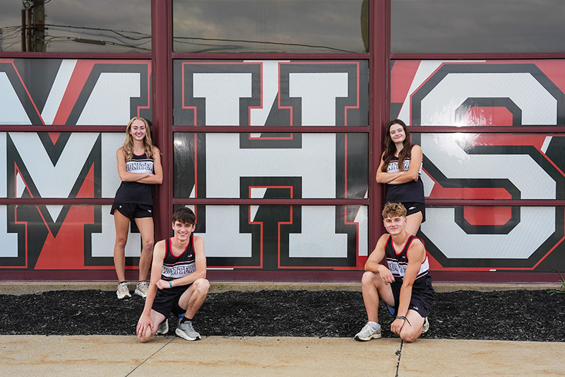 Four runners posing for a picture in front of school building
